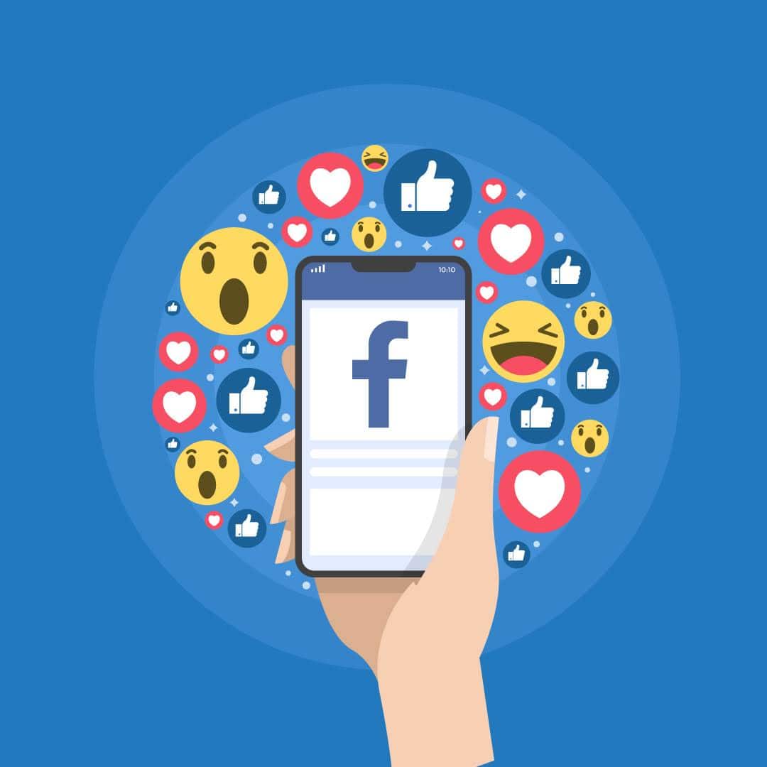 Hand holding phone with Facebook logo and reaction icons around on blue background
