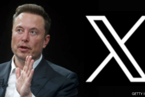 Elon Musk sat in front of his new X logo